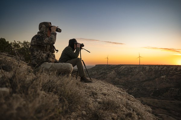 Two people using binoculars to look at wildlife in a canyon at sunset.