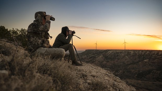 Two people using binoculars to look at wildlife in a canyon at sunset.