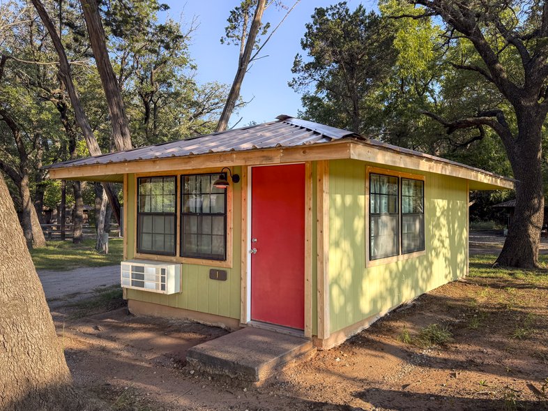 A yellow cabin with a red door named Cabin 1 at Abilene Sate Park.