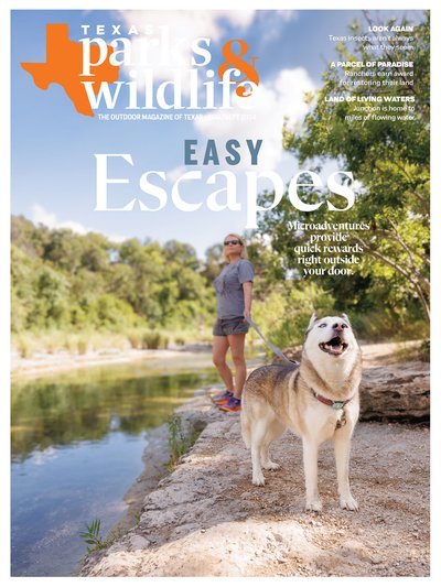 The cover of the August/September 2024 issue of Texas Parks & Wildlife magazine, which depicts a woman and her dog standing on the rocky shore of a river