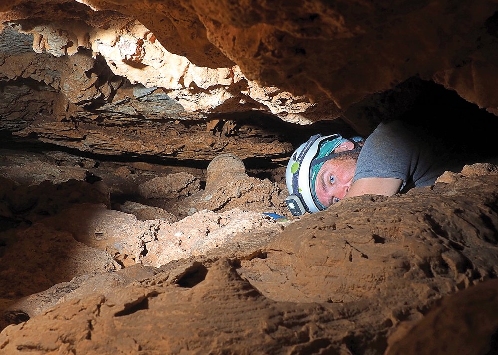A cave explorer on his belly moving through a tight crevice.
