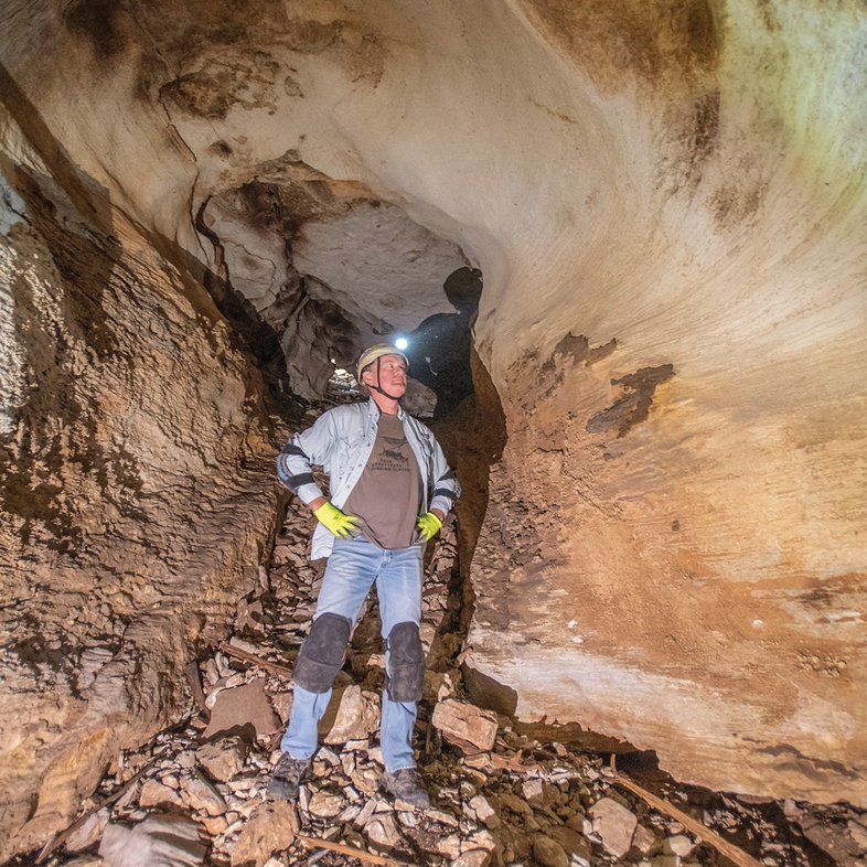 A caver looking up with a head lamp in side a cave with a wide stance and arms on his hips.