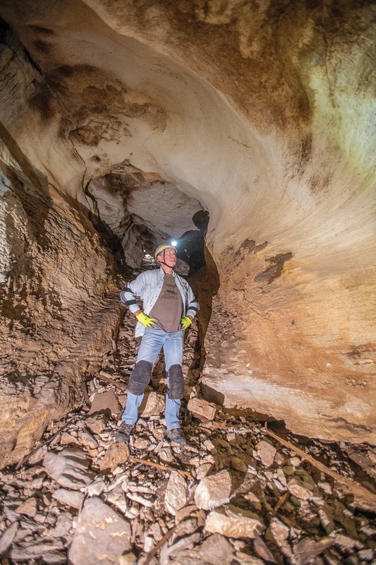 A caver looking up with a head lamp in side a cave with a wide stance and arms on his hips.