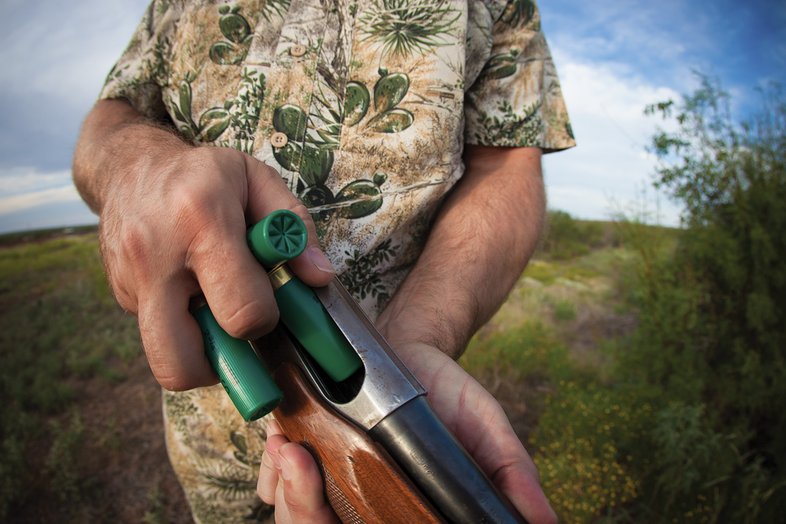 A close up of a person loading rounds into a gun.