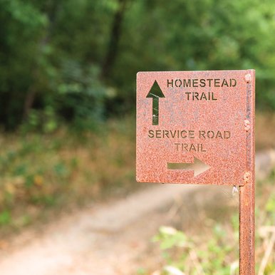 A directional sign showing the homestead trail is straight and the service road trail is to the right.