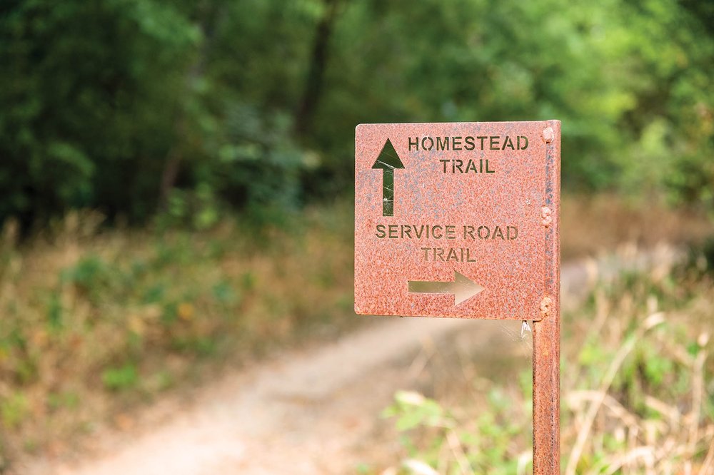 A directional sign showing the homestead trail is straight and the service road trail is to the right.