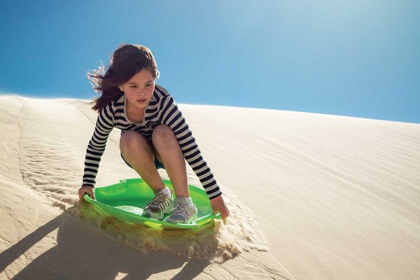 A girl on a sanddisc surfing the dunes.