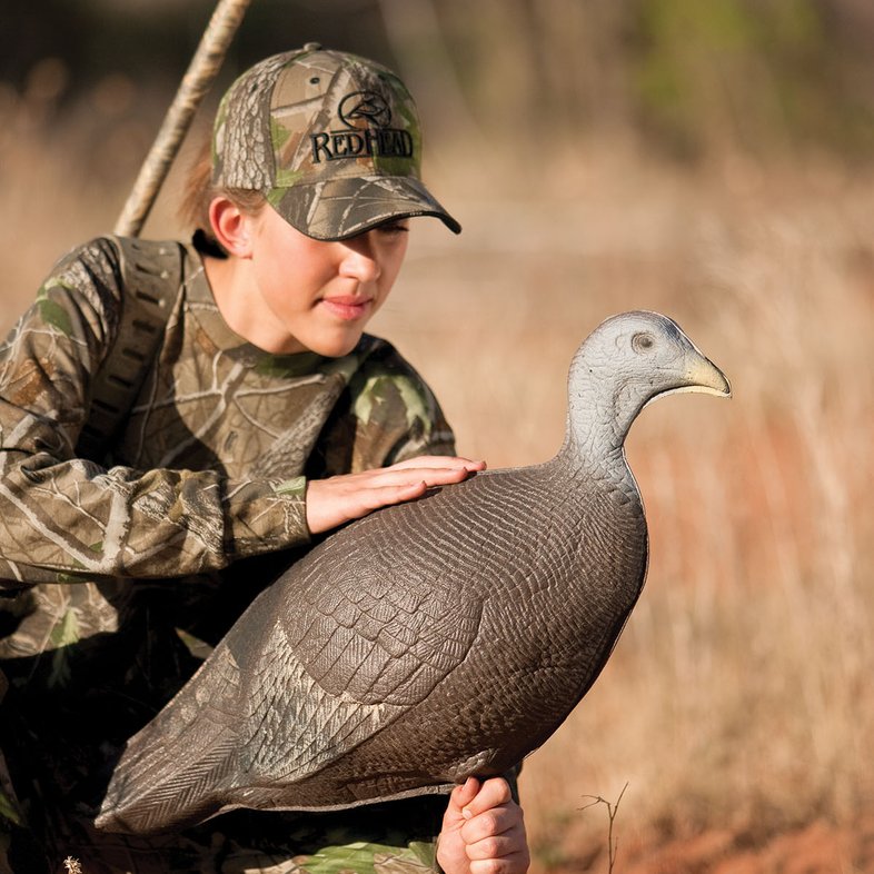 A person in a hat placing a turkey decoy.