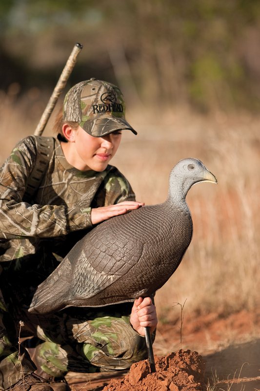 A person in a hat placing a turkey decoy.