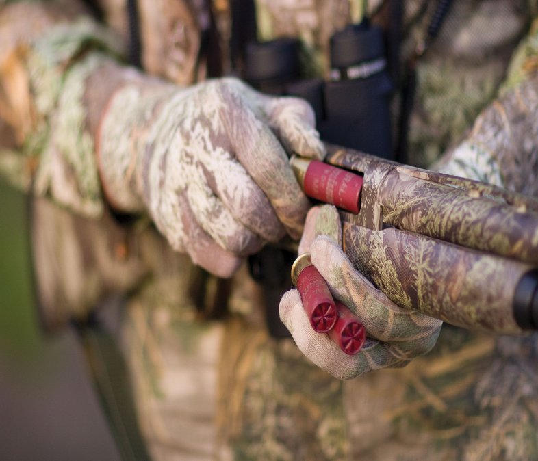 A person loading a camouflage gun with turkey rounds.