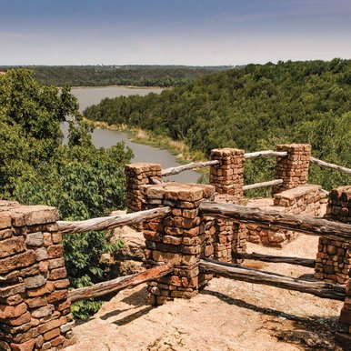 A trail overlook with a view of hills and a lake.