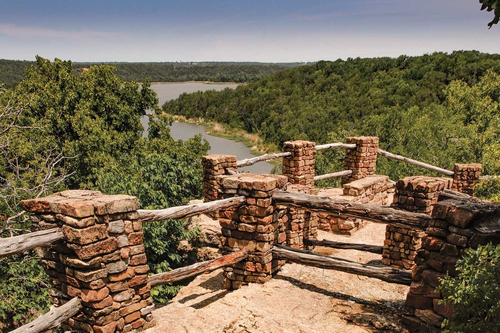 A trail overlook with a view of hills and a lake.