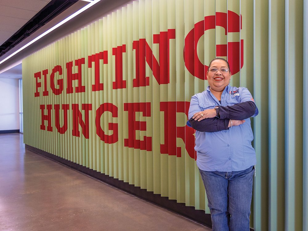 A volunteer standing in front of a a Fighting Hunger sign.