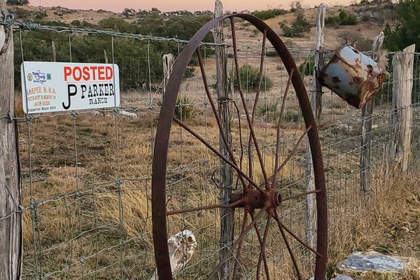 An old wagon wheel leaning against a wire fence.