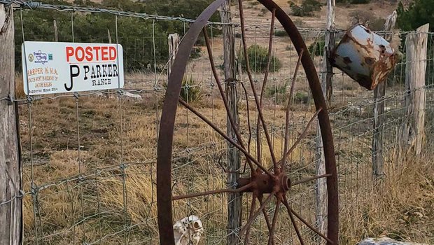 An old wagon wheel leaning against a wire fence.