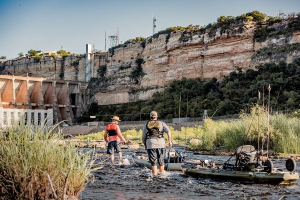 Anglers in the water near a dam.