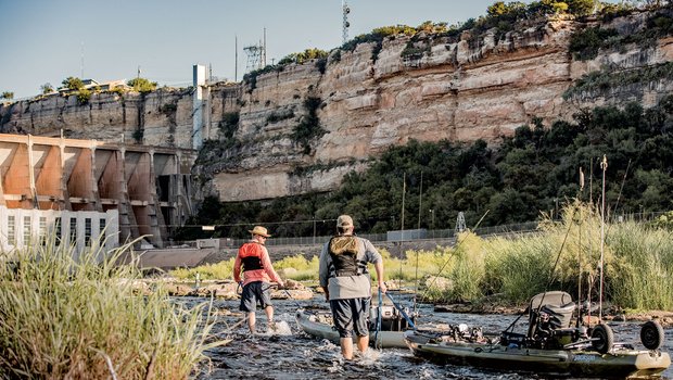 Anglers in the water near a dam.