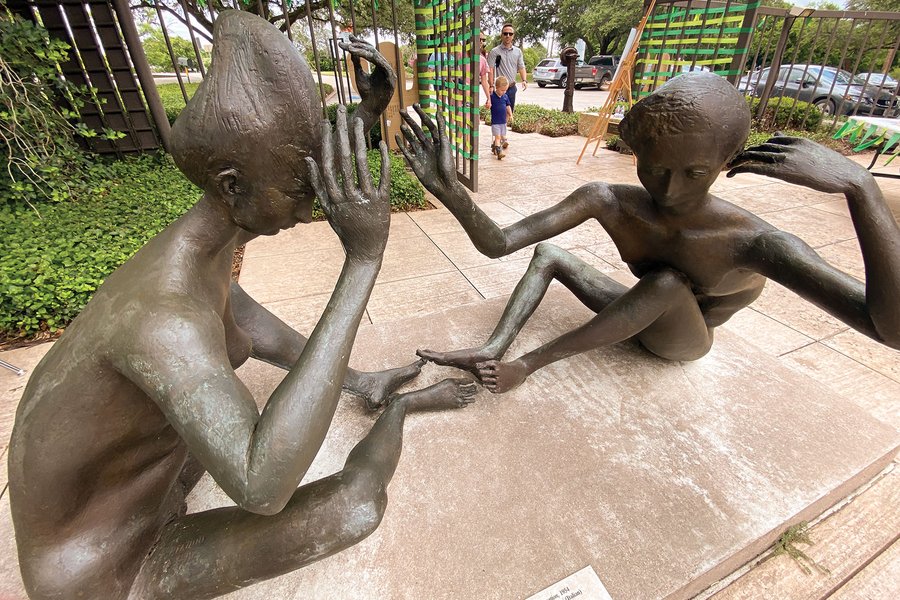 Bronze sculpture of two people sitting on the ground talking.