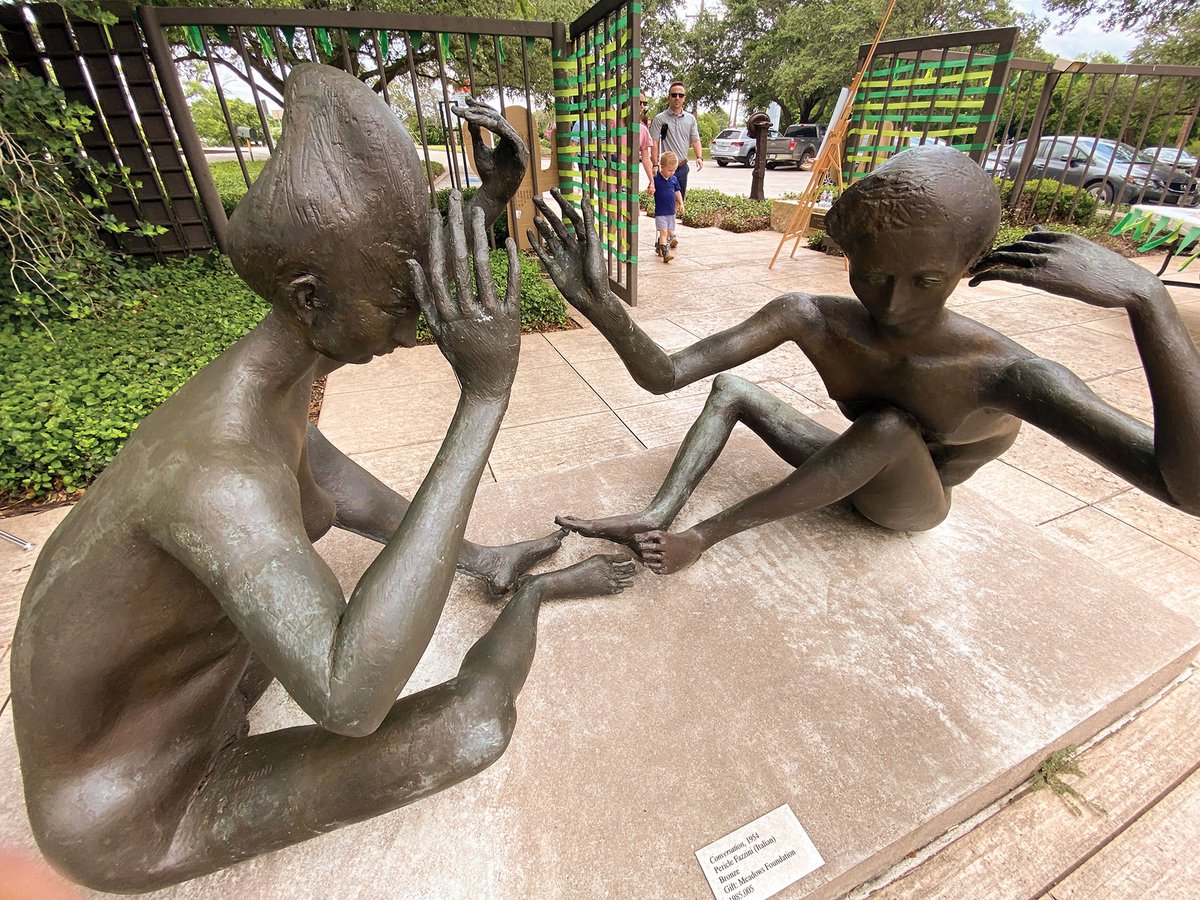 Bronze sculpture of two people sitting on the ground talking.