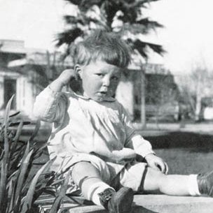 Black and White Photo of Clark Hubbs as a toddler sitting on a sidewalk