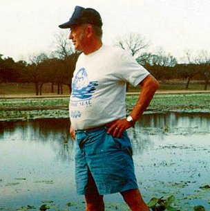 Clark Hubbs in baseball cap standing at the edge of water