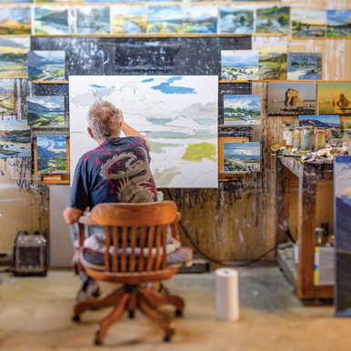 David Canton painting a landscape in a wooden swivel chair in his studio