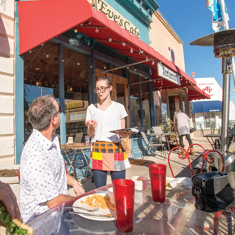 Server and Diner on a patio at Eve's Cafe in Lampasas Texas with blue restaurants front and red awning