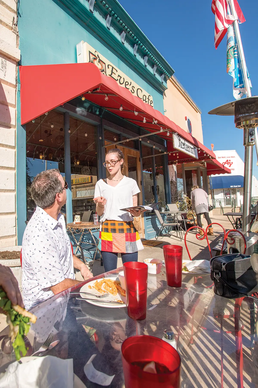 Server and Diner on a patio at Eve's Cafe in Lampasas Texas with blue restaurants front and red awning
