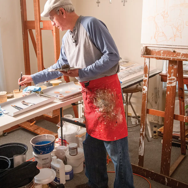 Fidencio Duran painting in his studio with a table holding paints and an easel with a canvas that is in progress