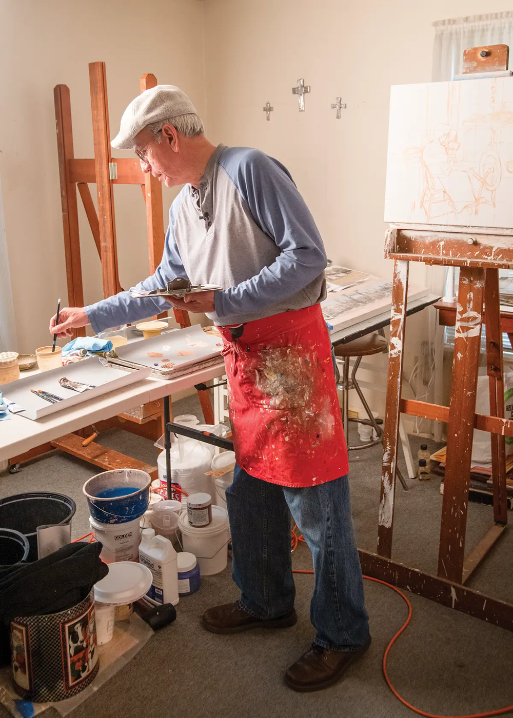 Fidencio Duran painting in his studio with a table holding paints and an easel with a canvas that is in progress