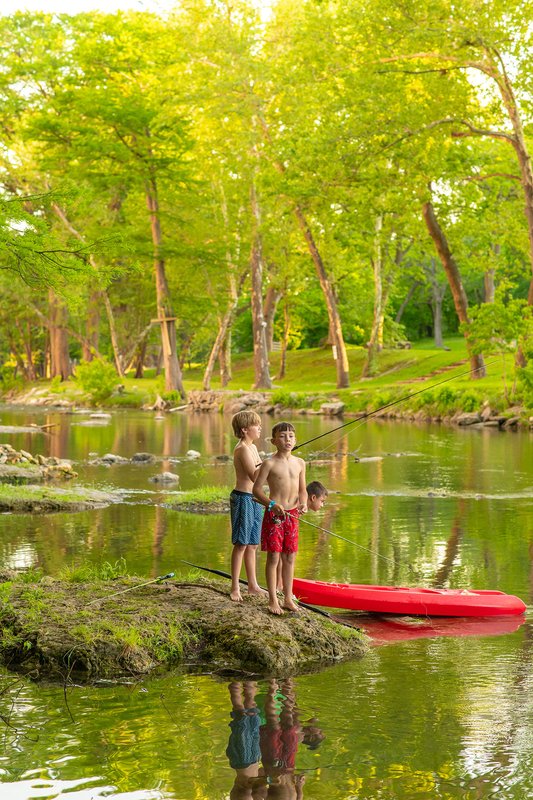 Two children river fishing next to a red boat at Camp Fimfo.