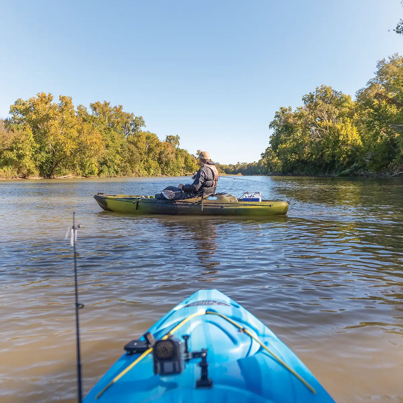 Front of blue kayak being launched into a river at a river access site with a yellow kayak on the river