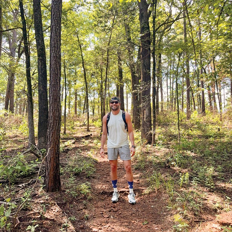 Man standing in the woods wearing a backpack and sunglasses