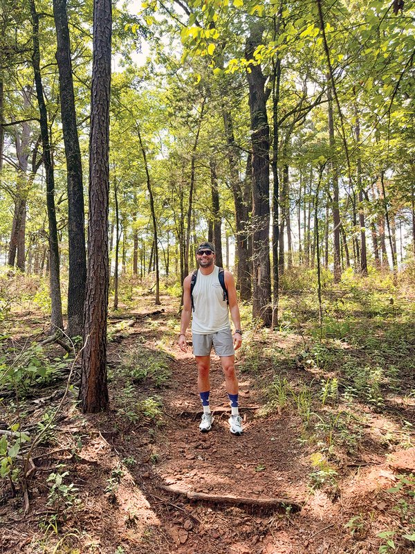 Man standing in the woods wearing a backpack and sunglasses