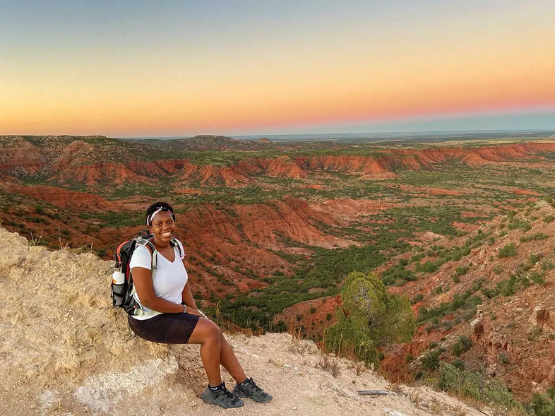 Irene Ogeto sitting on a slope overlooking canyons