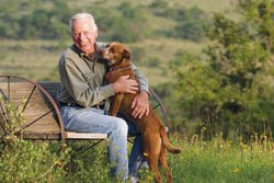 J. David Bamberger siting on a wagon wheel bench in a feild with his dog.