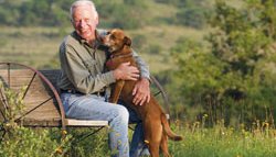 J. David Bamberger siting on a wagon wheel bench in a feild with his dog.