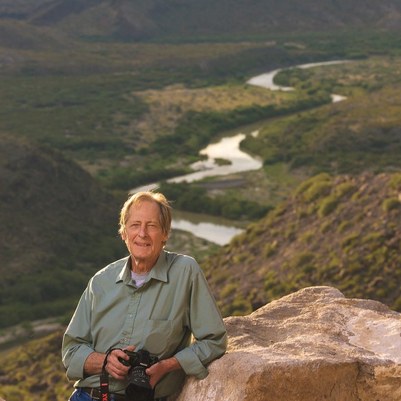 Photographer Jim Bones leans against a boulder with a river behind him in Big Bend.