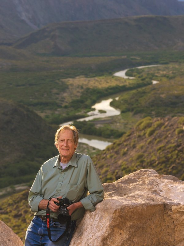 Photographer Jim Bones leans against a boulder with a river behind him in Big Bend.