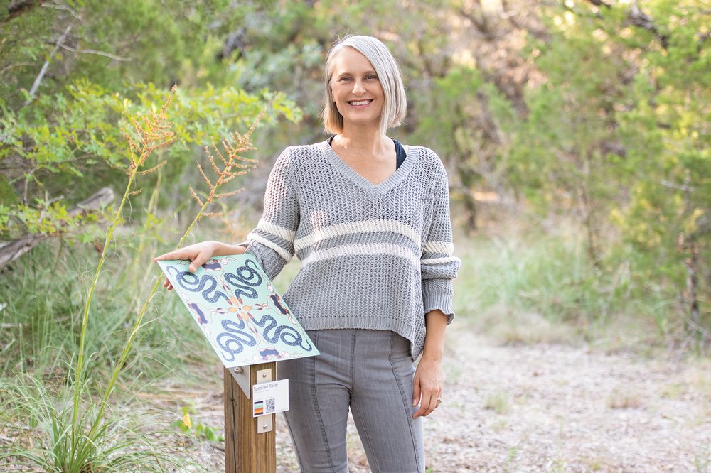 Juliet Whitsett standing next to her art work displayed on a park trail.