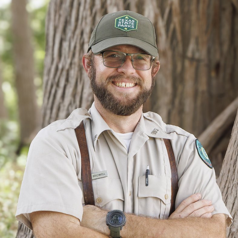 Kelby Birdwell standing with arms crossed in front of a tree.