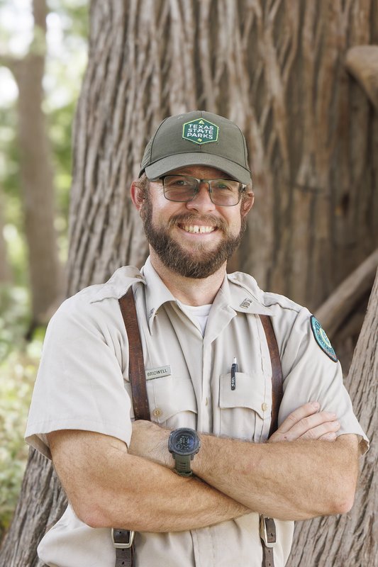 Kelby Birdwell standing with arms crossed in front of a tree.