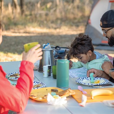 Two adults and a child sitting at a picnic table after finishing a meal. the child is looking at a map.