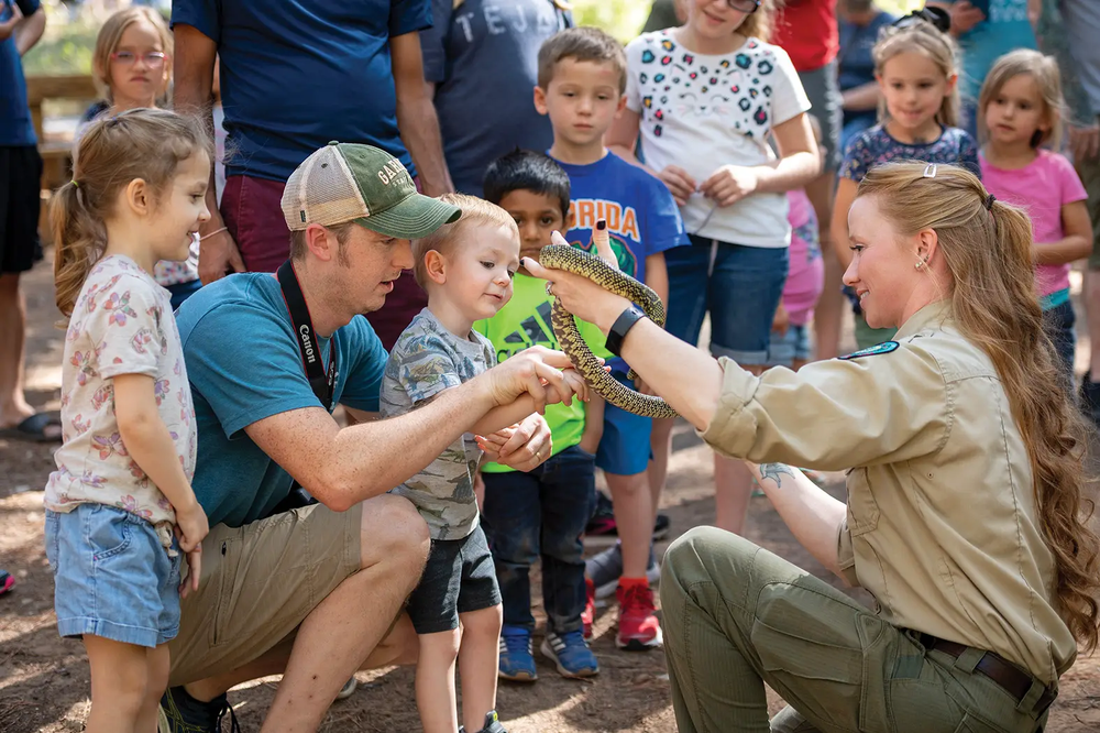A TPWD staff member squatting down showing a snake to a crowd of children and adults