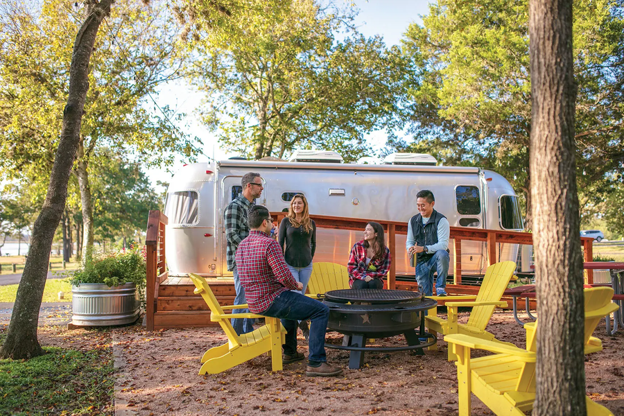 Lake Bastrop North Shore Park 5 people gathered around a fire pit with yellow Adirondack chairs and an RV in the background