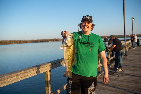 Man holding a fish by its mouth on a fishing pier.
