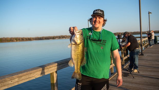 Man holding a fish by its mouth on a fishing pier.