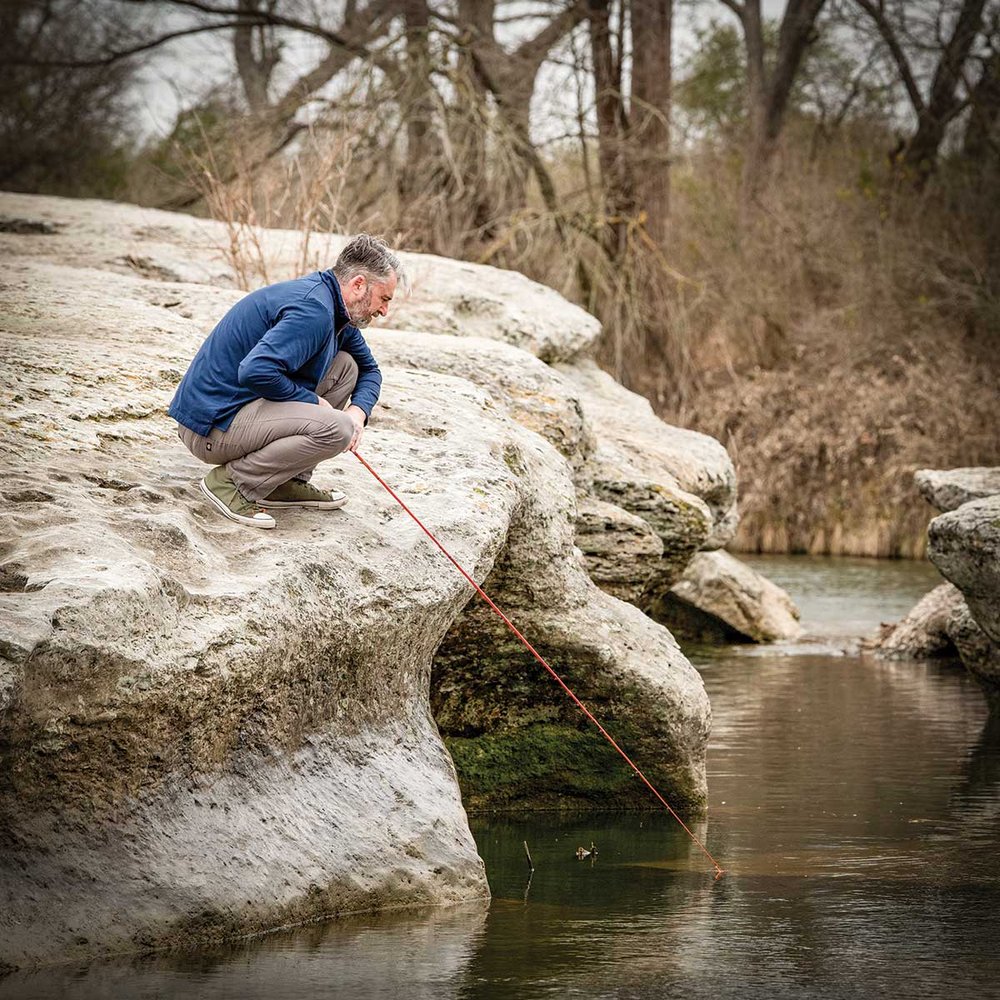 Man leaning over a rock formation while fishing.