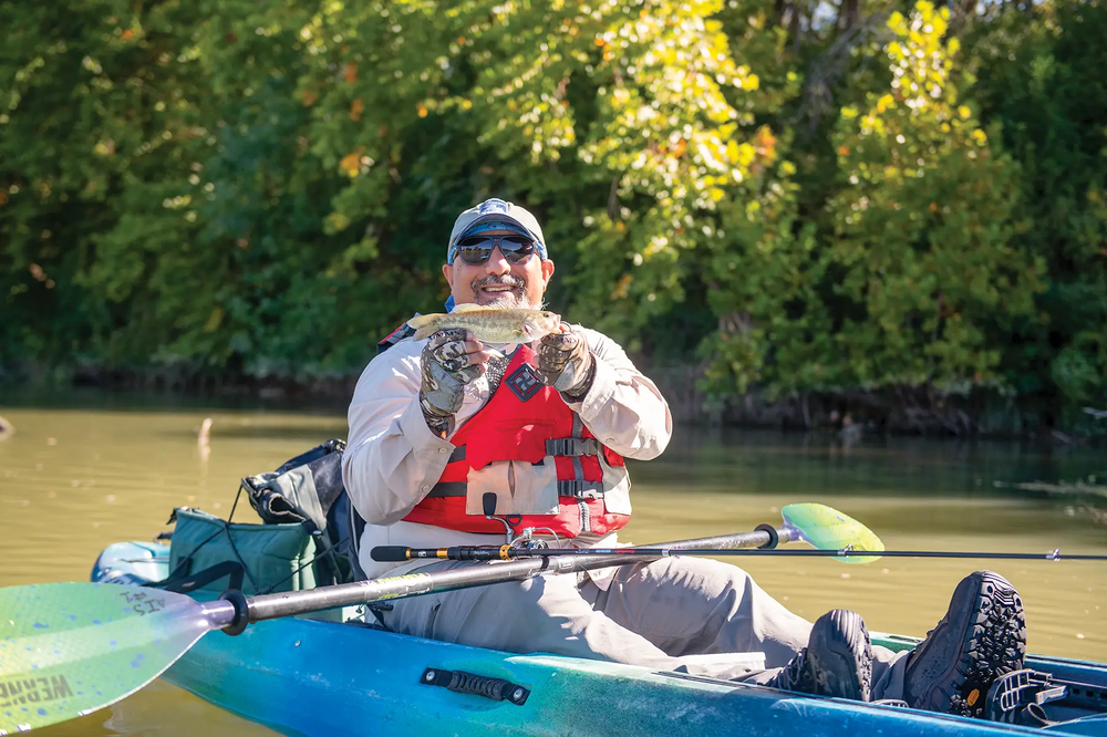 Man showing a fish he caught from his kayak with rod and paddle across his lap