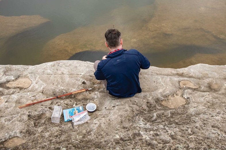 Man sitting on rock with fishing gear.